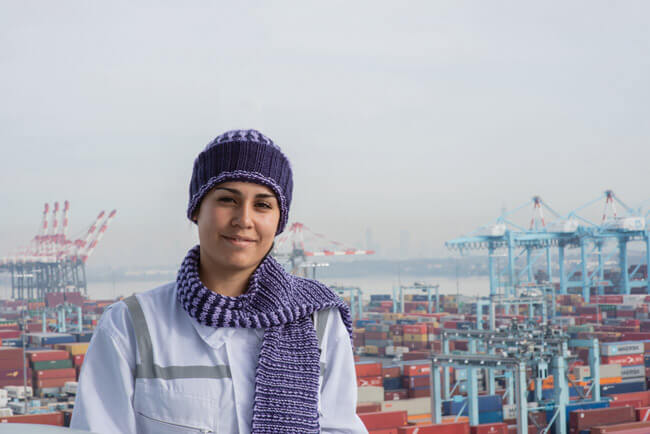 white woman in purple scarf in front of ship yard